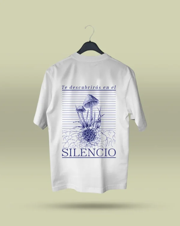 Camiseta blanca unisex con ilustración artística de hongos y raíces, acompañada de la frase poética Te descubrirás en el silencio. Ropa original hecha en Colombia con mensajes reflexivos y diseño exclusivo para quienes buscan prendas únicas con significado. Con envío a todo Colombia