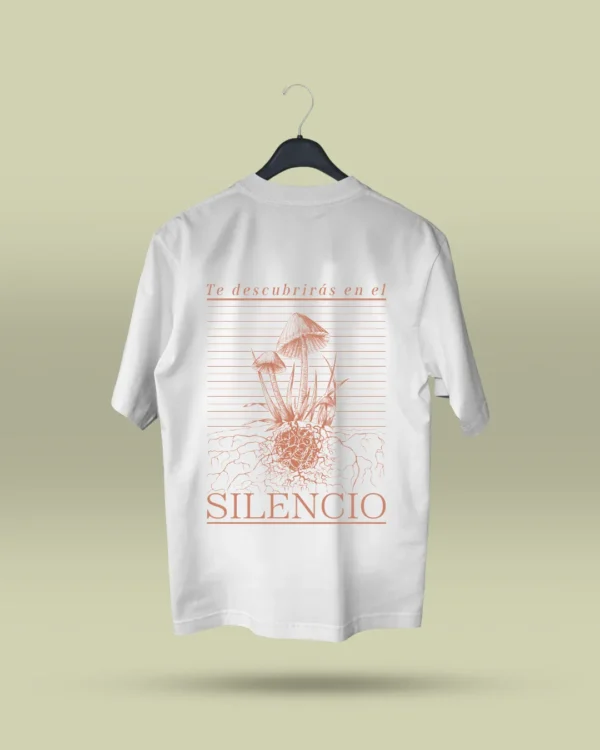 Camiseta blanca unisex con ilustración artística de hongos y raíces, acompañada de la frase poética Te descubrirás en el silencio. Ropa original hecha en Colombia con mensajes reflexivos y diseño exclusivo para quienes buscan prendas únicas con significado. Con envío a todo Colombia