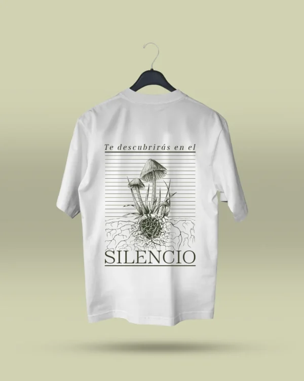 Camiseta blanca unisex con ilustración artística de hongos y raíces, acompañada de la frase poética Te descubrirás en el silencio. Ropa original hecha en Colombia con mensajes reflexivos y diseño exclusivo para quienes buscan prendas únicas con significado. Con envío a todo Colombia