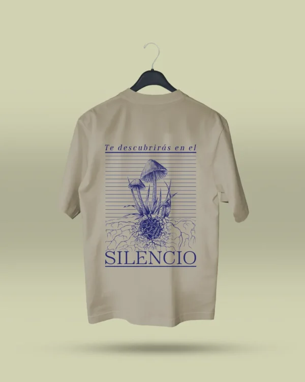 Camiseta beige unisex con ilustración artística de hongos y raíces, acompañada de la frase poética Te descubrirás en el silencio. Ropa original hecha en Colombia con mensajes reflexivos y diseño exclusivo para quienes buscan prendas únicas con significado. Con envío a todo Colombia