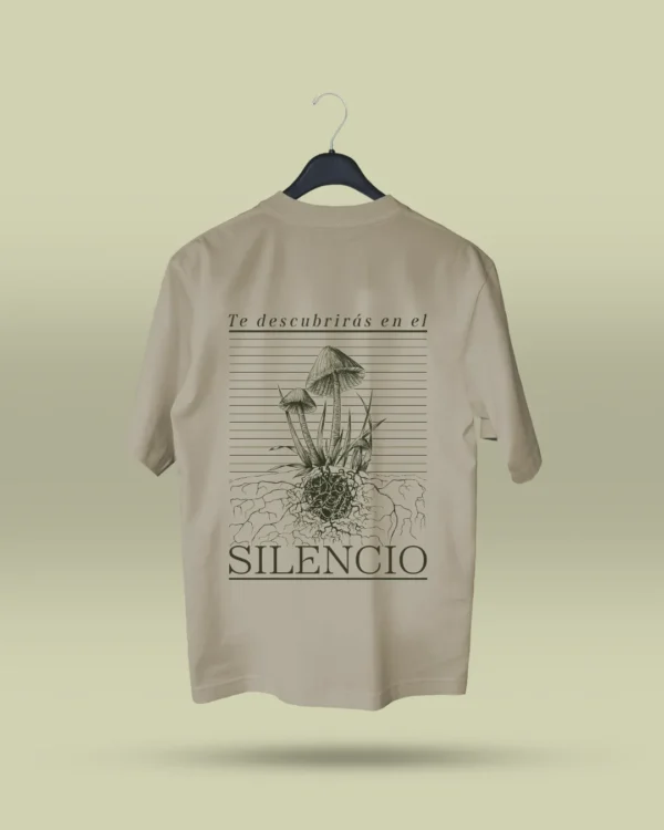 Camiseta beige unisex con ilustración artística de hongos y raíces, acompañada de la frase poética Te descubrirás en el silencio. Ropa original hecha en Colombia con mensajes reflexivos y diseño exclusivo para quienes buscan prendas únicas con significado. Con envío a todo Colombia
